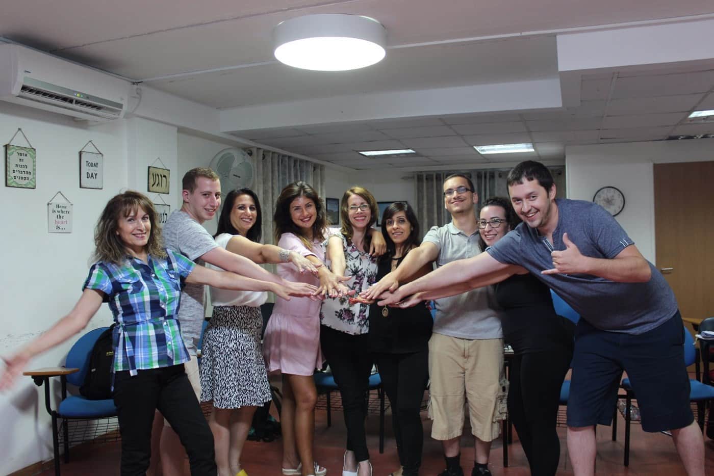 תמונה קבוצתית של משתתפי קורס NLP מחייכים ומשלבים ידיים בכיתת הלימוד